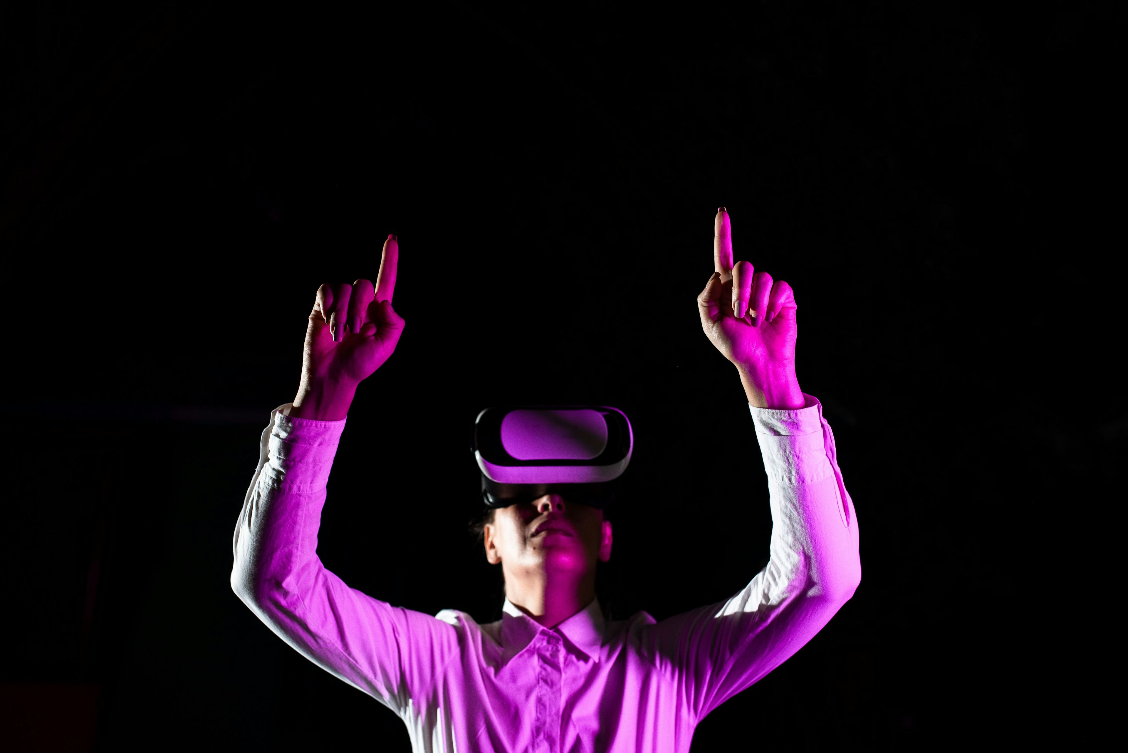 Woman wearing a VR headeset pointing up with both hands.