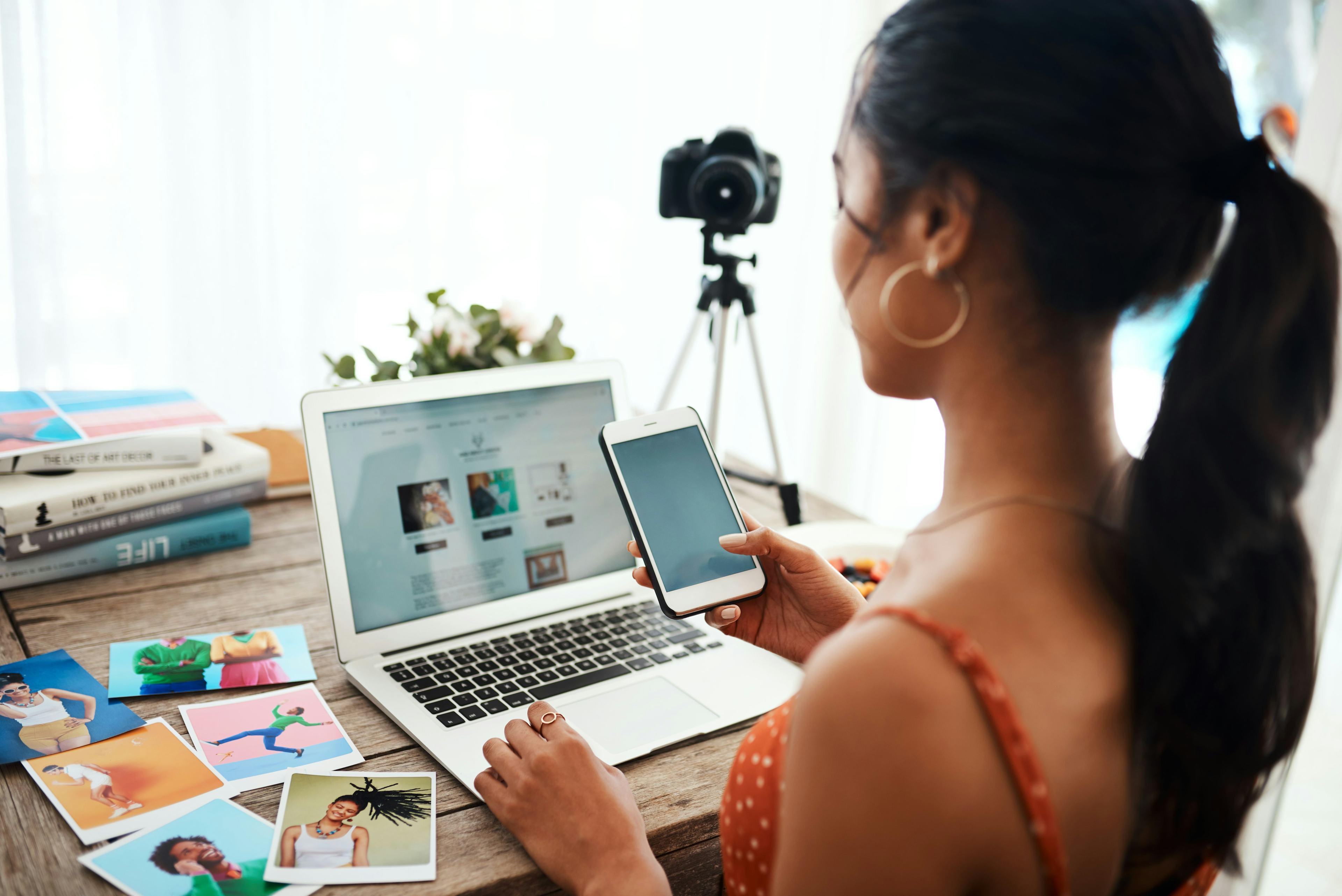 Young woman using laptop and camera to create content.