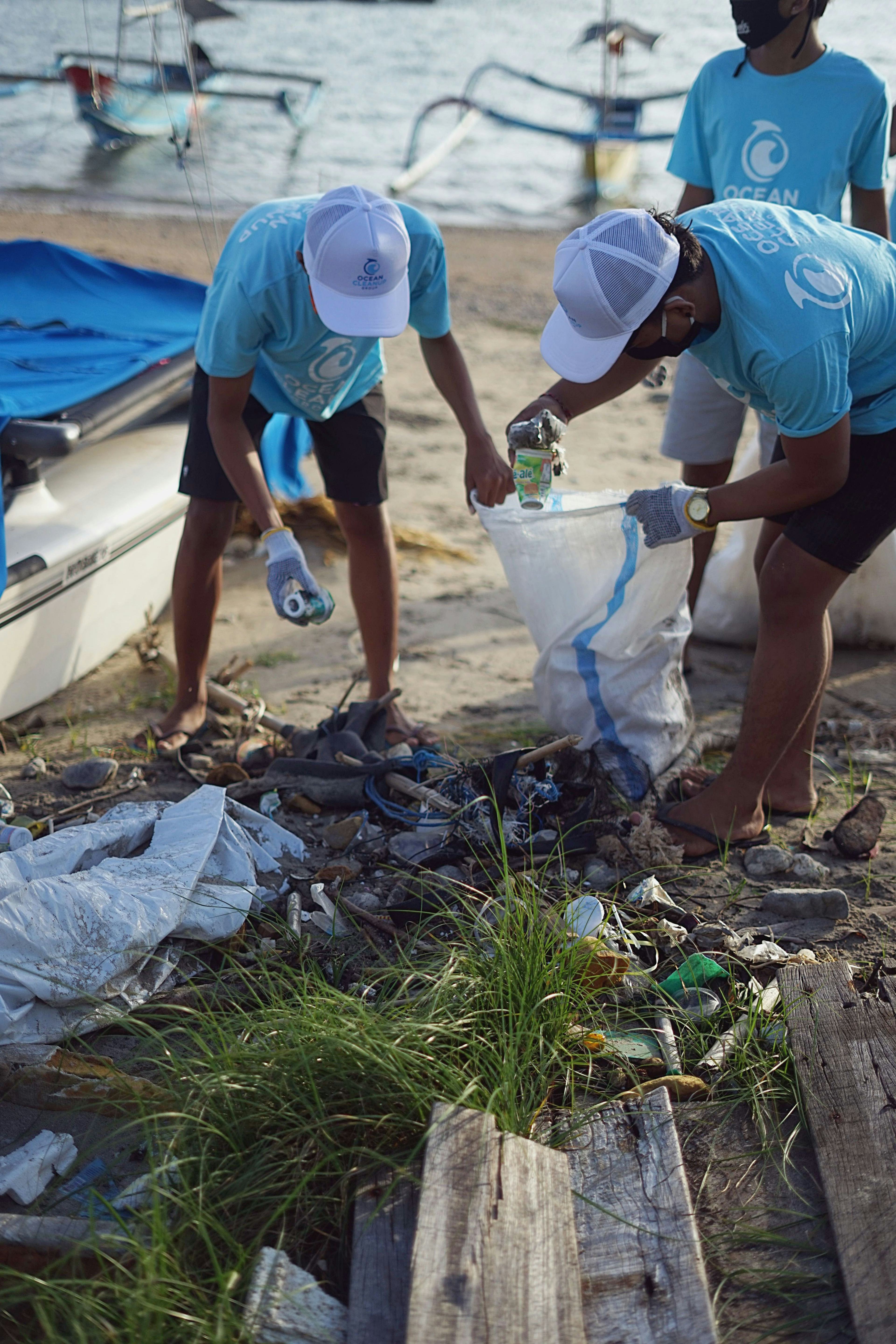 people dressed in blue shirts and black shorts with a plastic bag doing a trash cleanup of a sandy beach