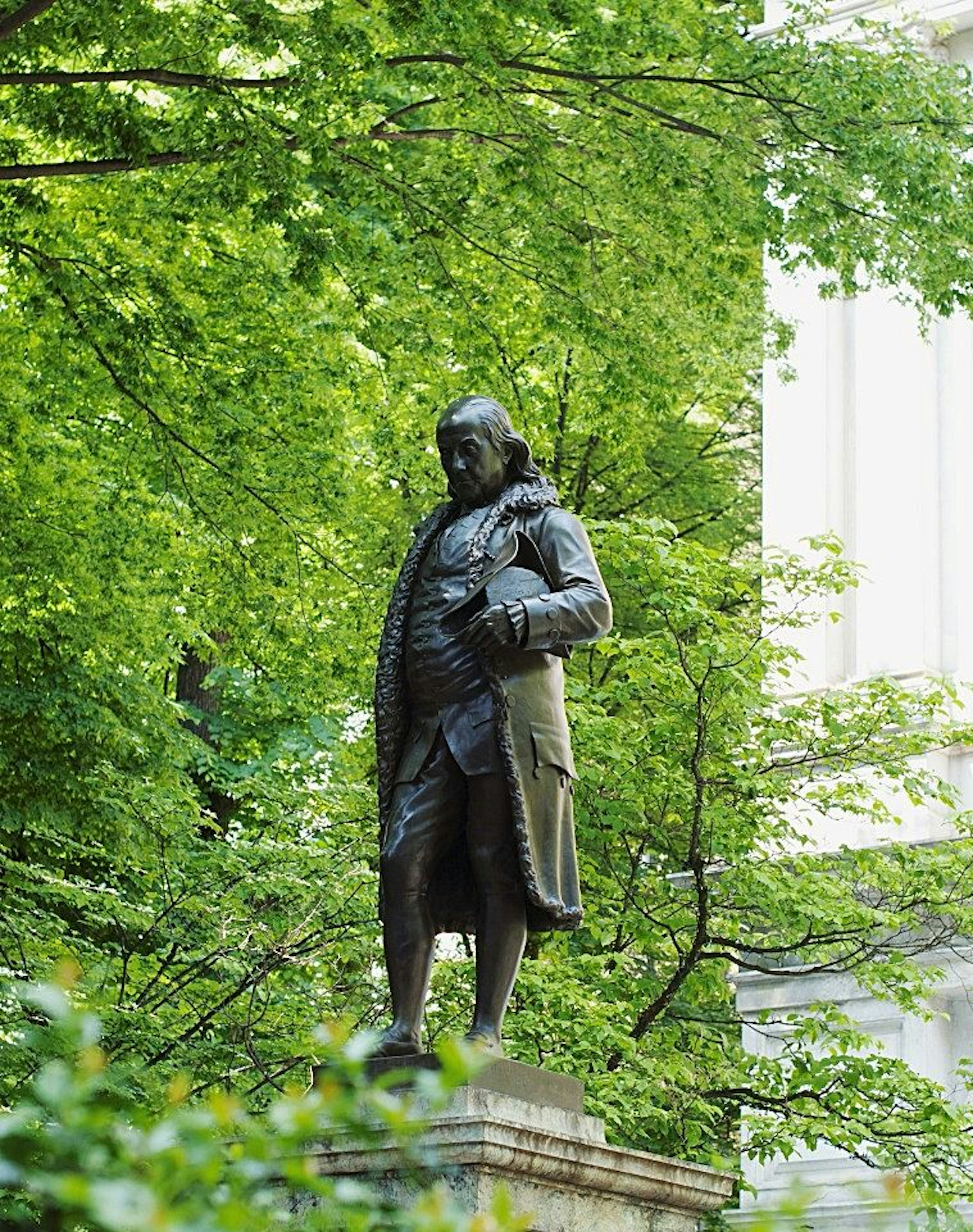 statue of Benjamin Franklin with green, leafy trees in the backdrop